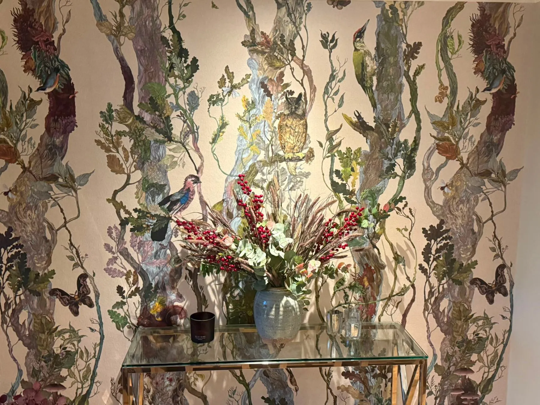 Illustrated woodland wallpaper hung in a hallway behind a glass console table