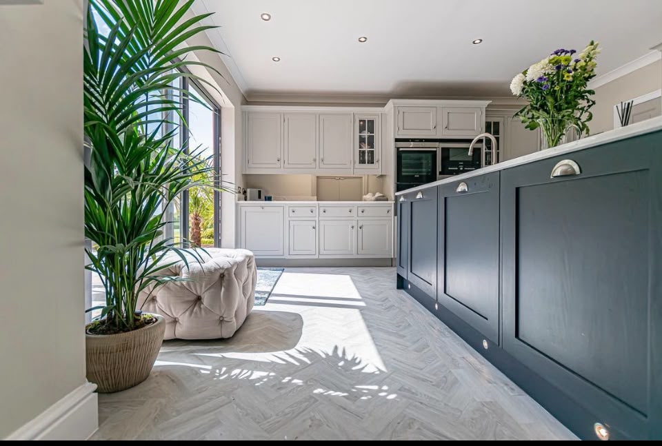 Charcoal hand painted kitchen island with pale cabinetry and a bright herringbone floor