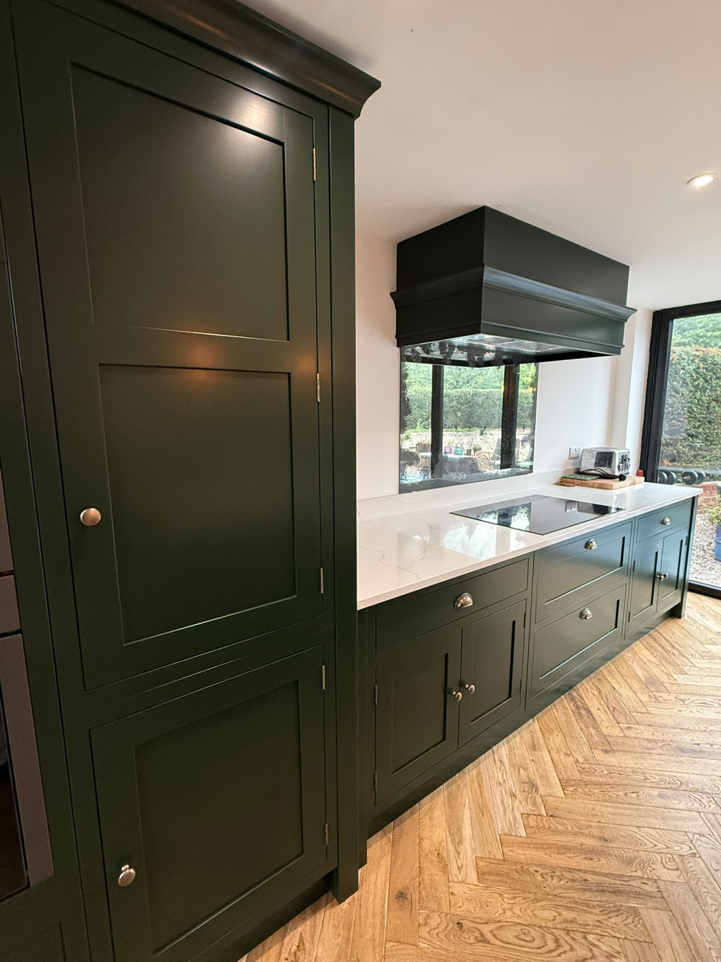 Dark green hand painted kitchen cookline with tall pantry cabinetry and quartz worktop
