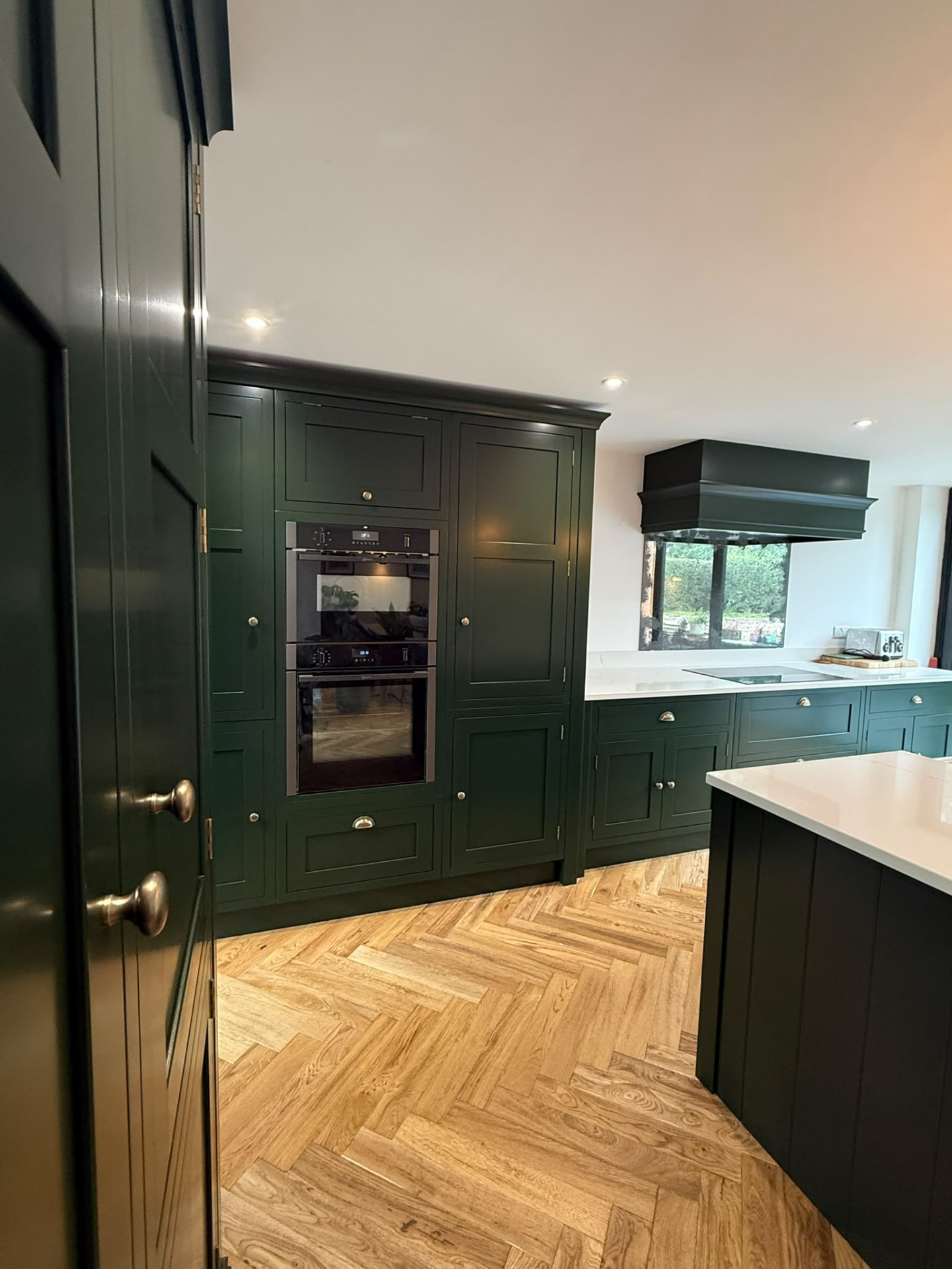 Hand painted green floor-to-ceiling kitchen cabinets surrounding integrated double ovens