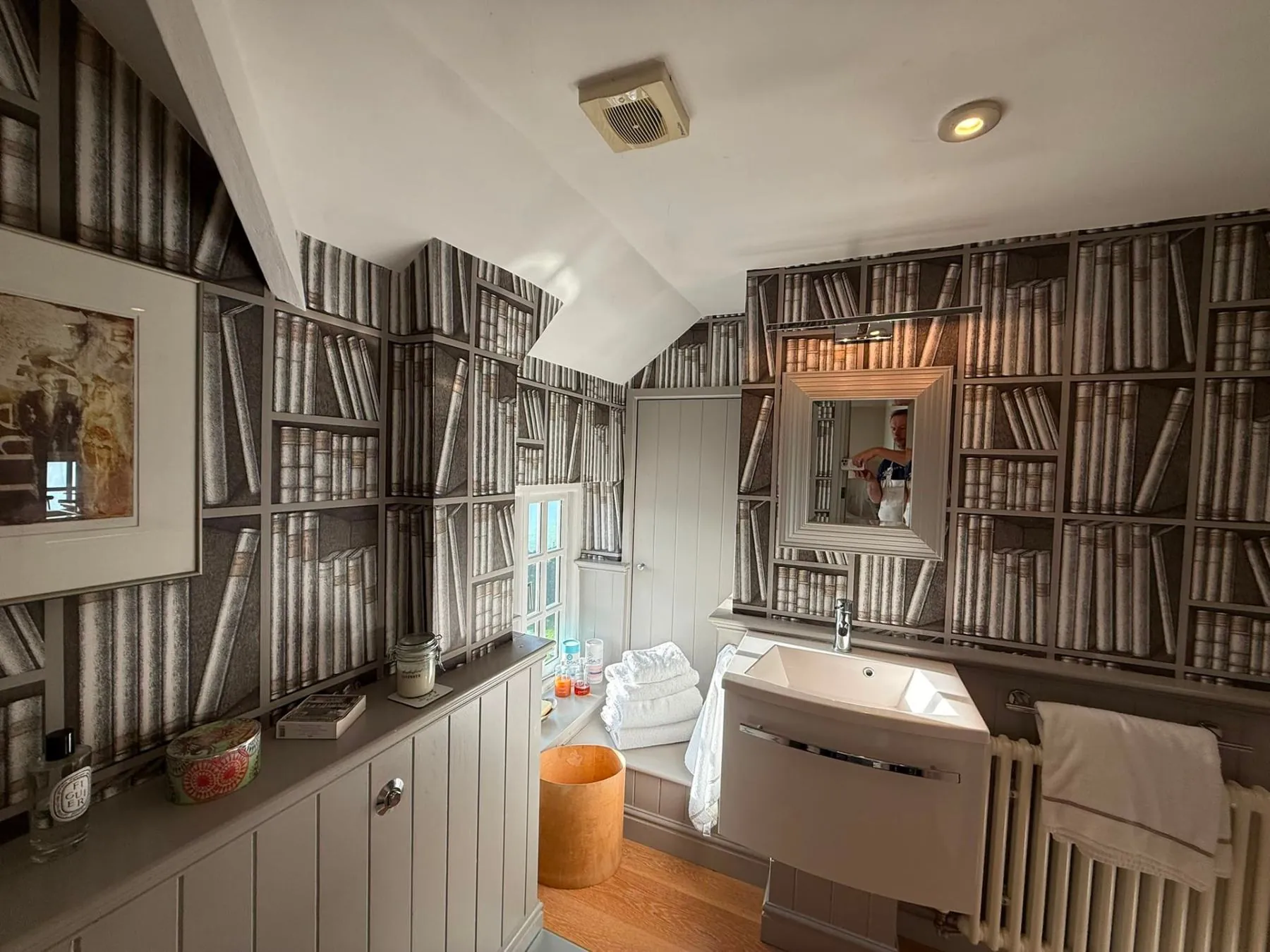 Bookshelf print wallpaper hung in a cottage bathroom with sloped ceilings