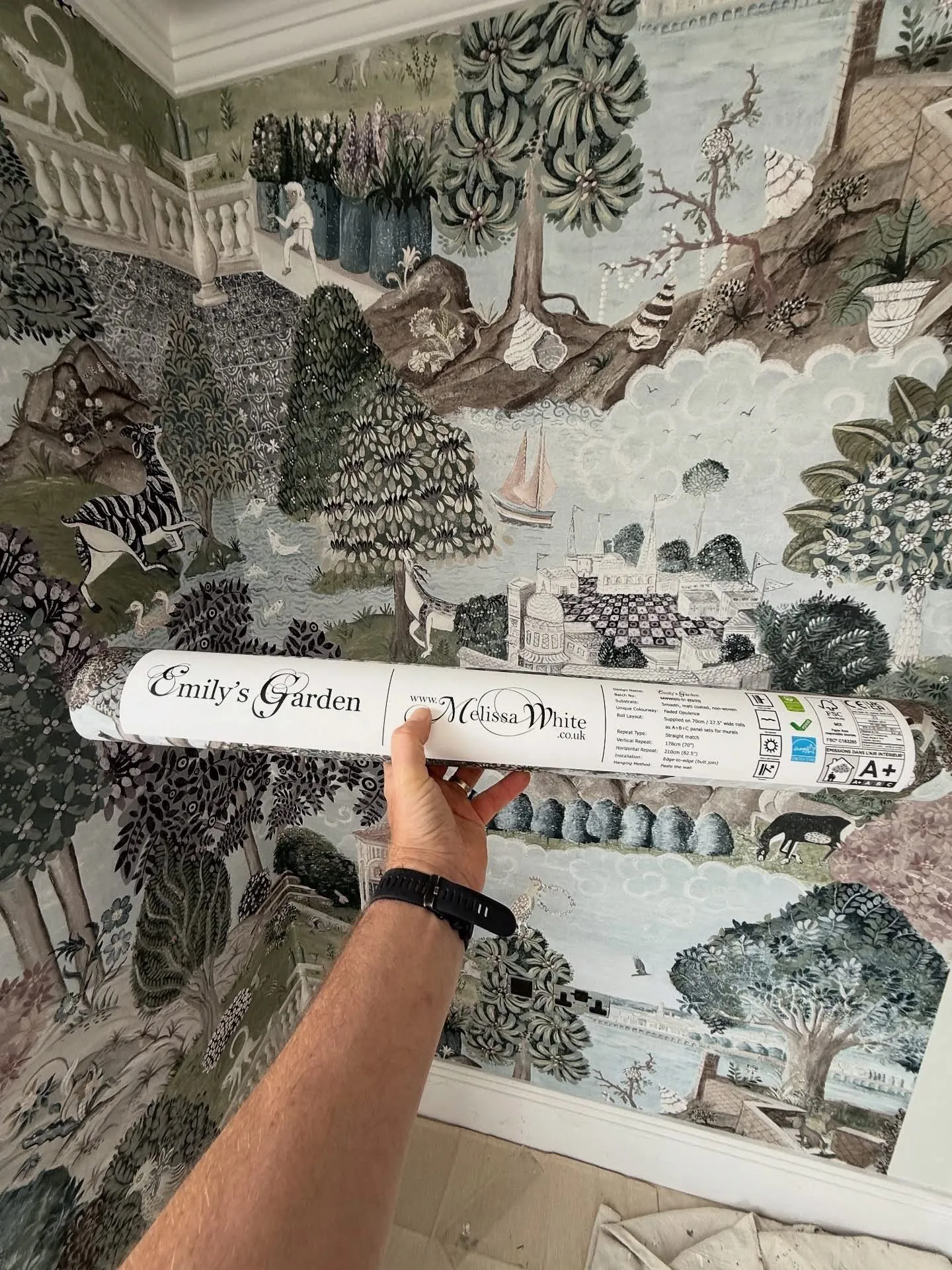 Hand-illustrated panoramic garden mural wallpaper hung across a corner of a room