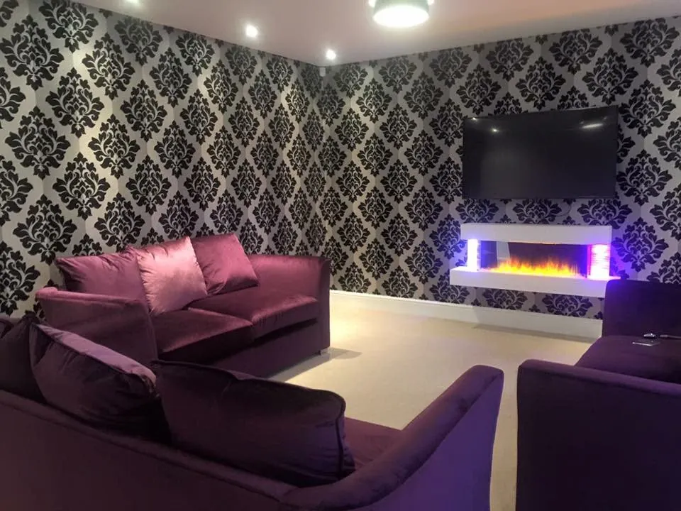 Silver and black damask wallpaper hung in a media room with a purple velvet sofa
