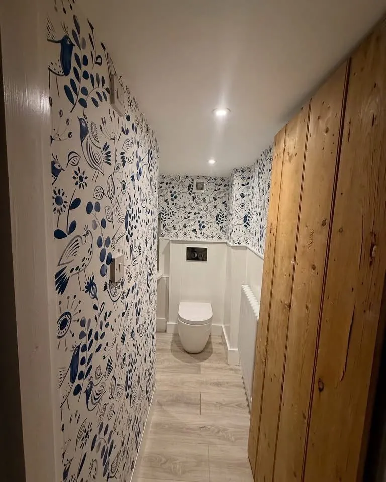 Blue folk bird wallpaper in a compact cloakroom above white panelling
