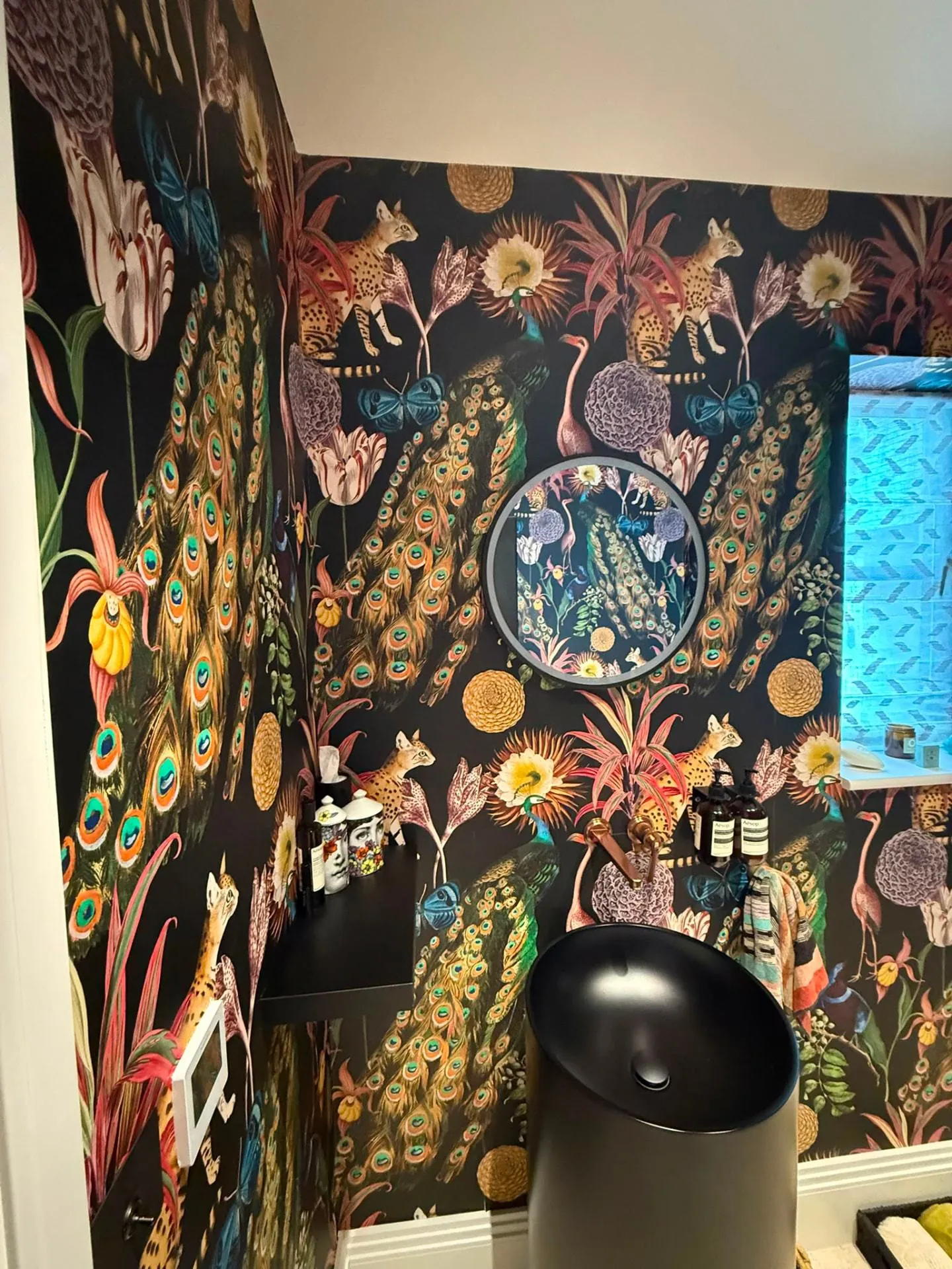 Dark exotic peacock wallpaper hung in a small cloakroom with sloped ceiling