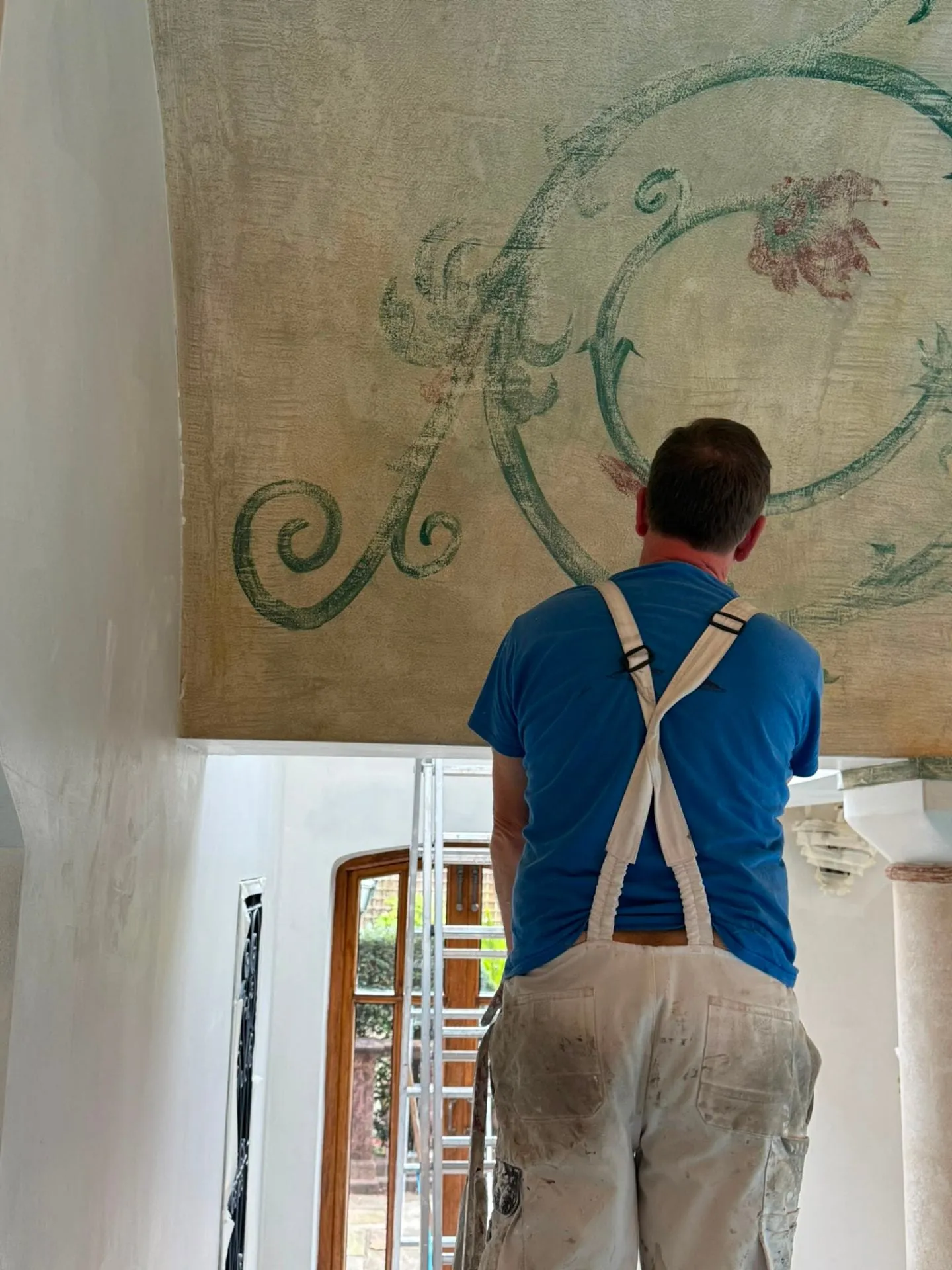 Decorator hand finishing a decorative ceiling mural from a ladder