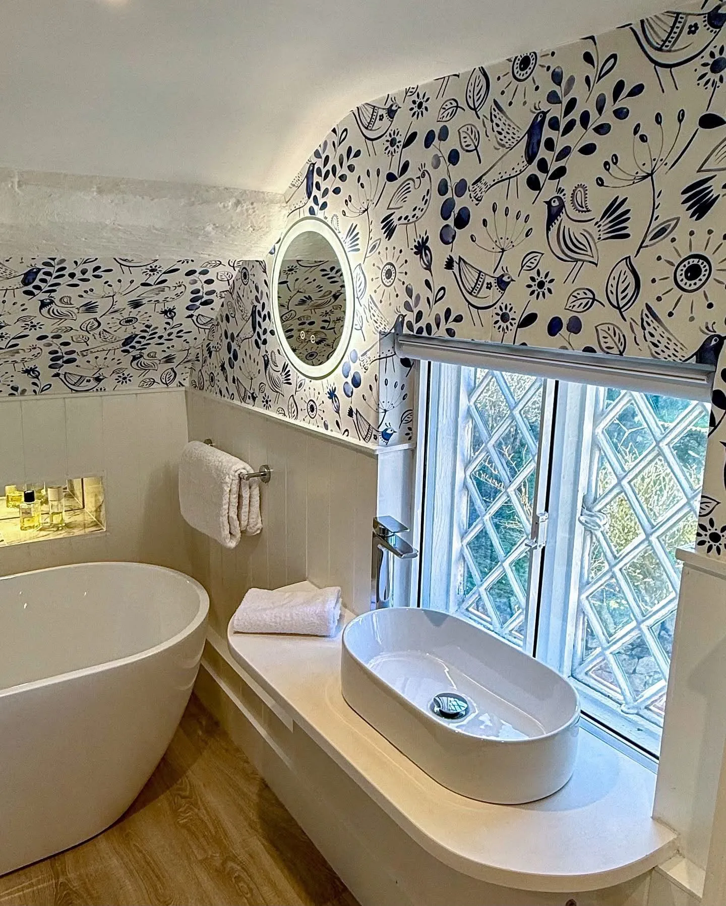 Blue folk bird wallpaper above painted panelling in a cottage bathroom