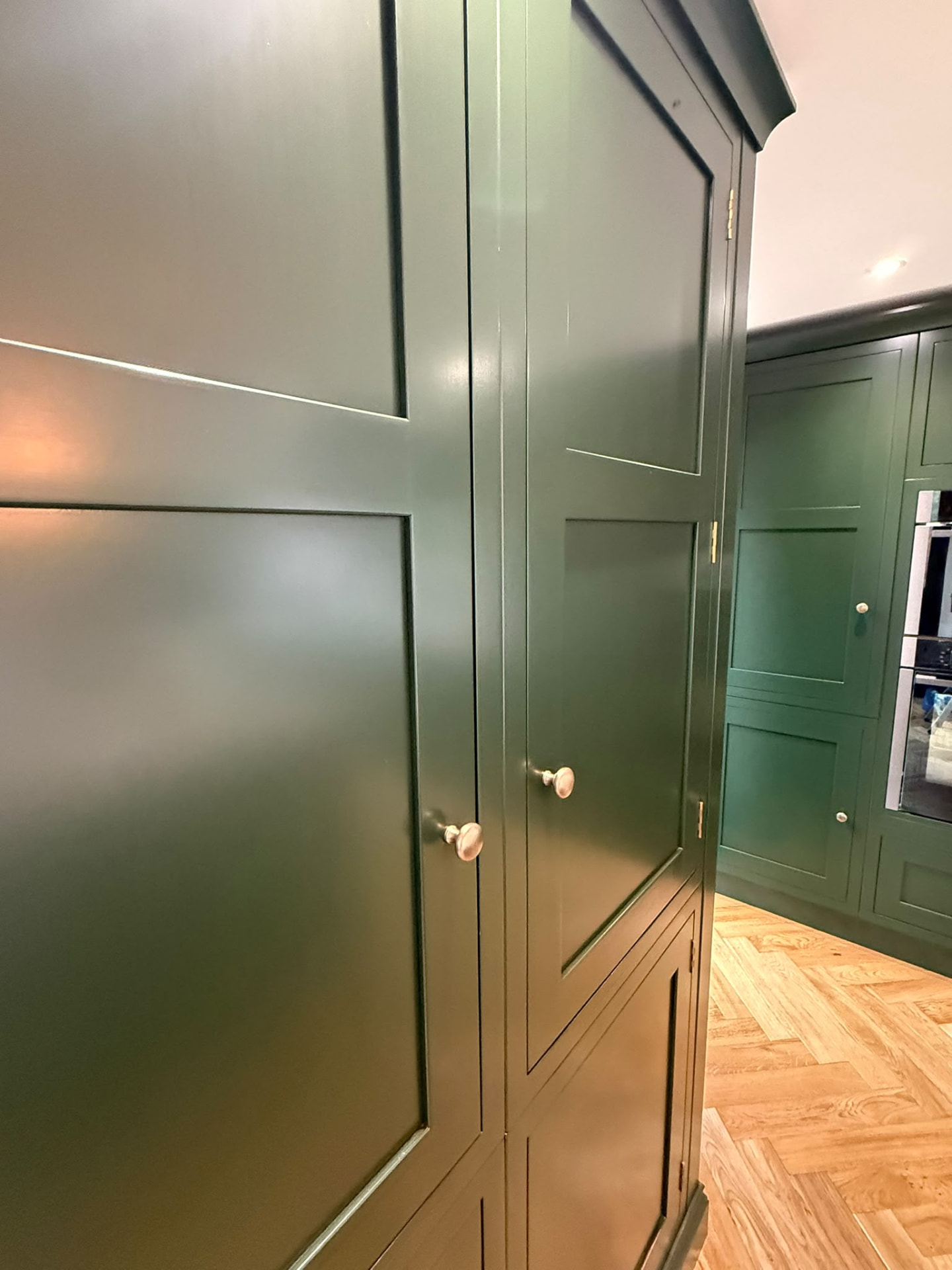 Close detail of smooth dark green hand painted kitchen cabinet doors and brass knobs